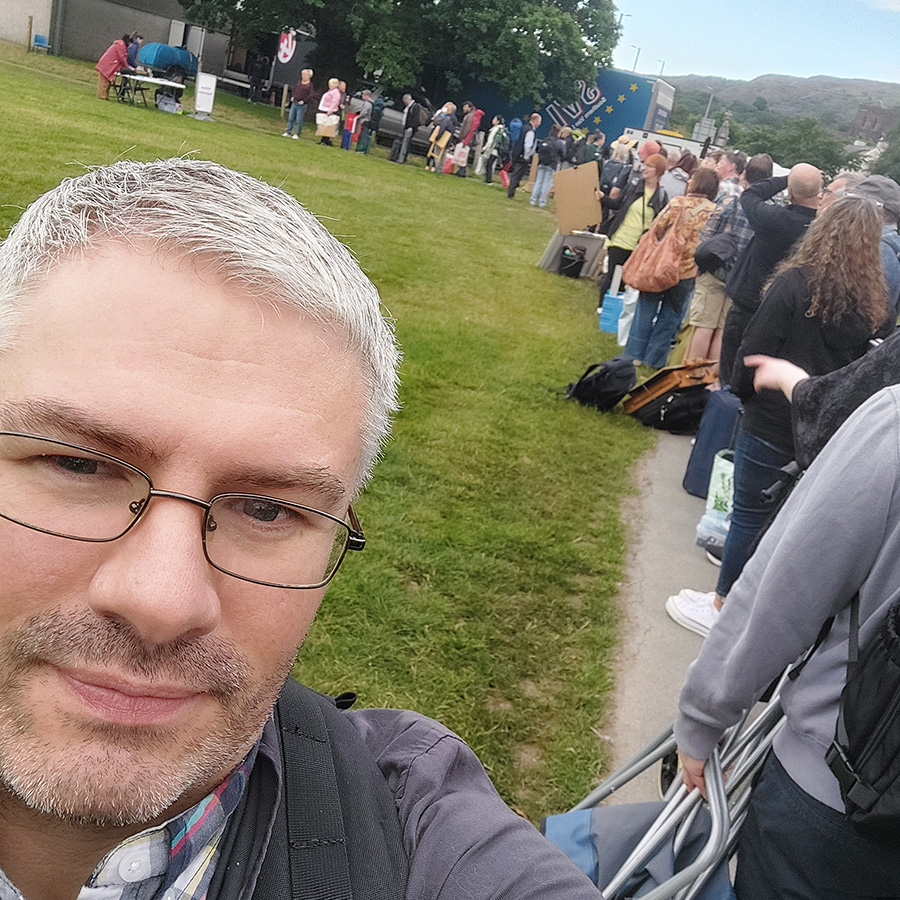 Photograph of artists queuing to register on a field in the morning sun.